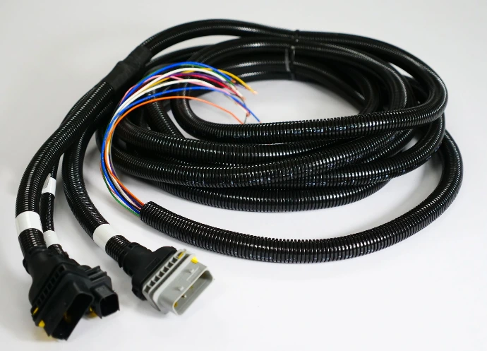 Long cable assemble coiled up and covered in protective plastic conduit. One end is open wire and the other has three overmoulded plugs attached