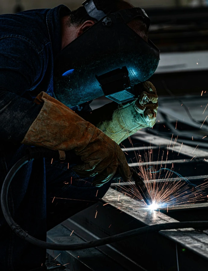 A welder working on a piece of metal, welding cable visible