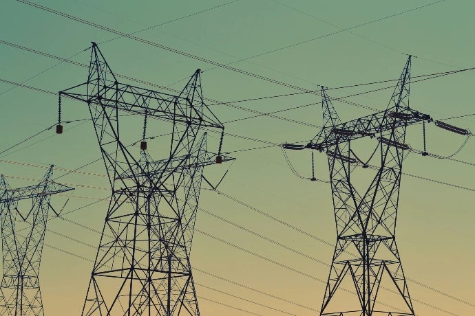 Black power transmission towers, with high voltage cables criss crossing against a green sky