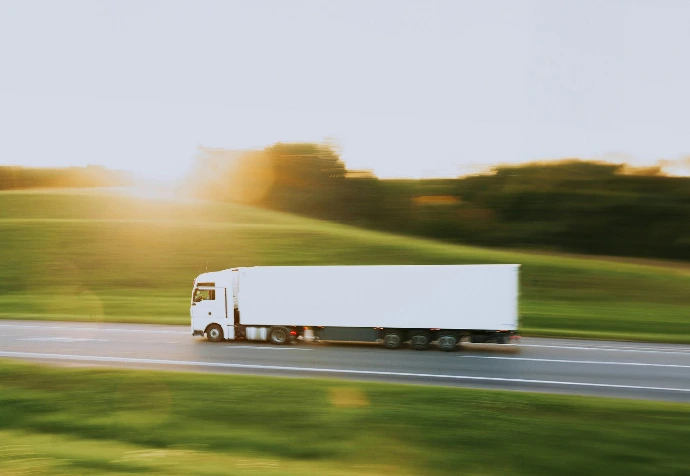 Long white commercial lorry driving down the motorway with sun shining