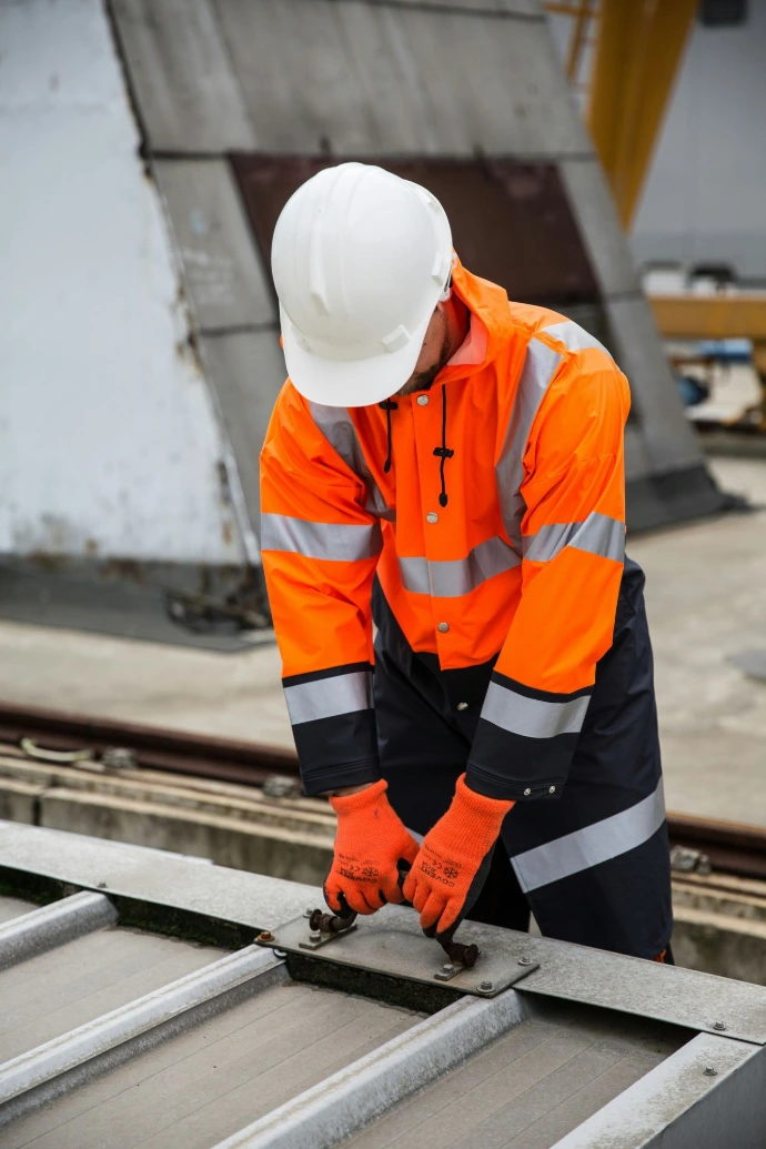 A man in Hi- vis and a hard hat with gloves on doing construction work